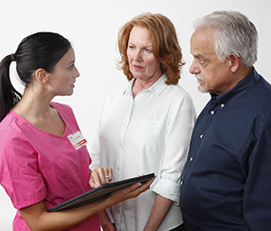 Healthcare provider with electronic tablet talking to woman and man.