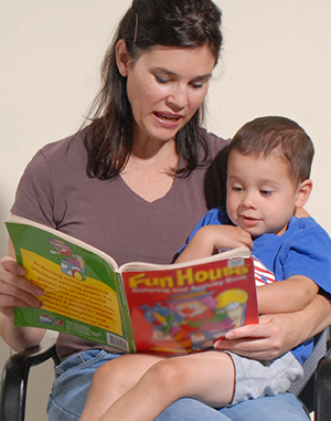 Woman holding preschool boy in lap, reading.