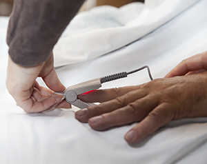 Primer plano de las manos de un proveedor de atención médica que colocan un pulsioxímetro en el dedo de un hombre.