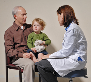 Niño sentado en la falda de un hombre mientras el hombre habla con el proveedor de atención médica.